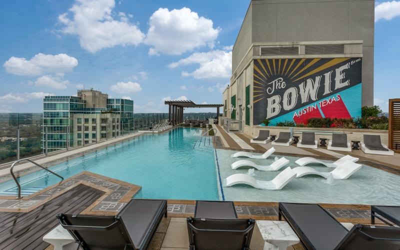 a rooftop pool with a sun-shelf and chairs